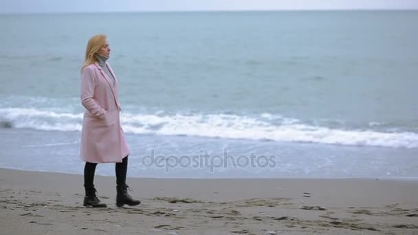 Gelukkig meisje in roze jas in de buurt van de zee tijdens een storm. sterke wind. — Stockvideo