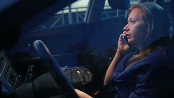 Девушка вечером разговаривает по телефону, сидя в машине — стоковое видео