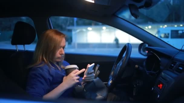Дівчина ввечері розмовляє по телефону, сидячи в машині — стокове відео