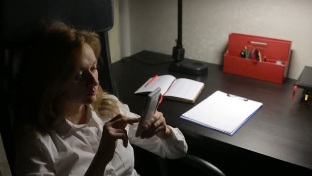 Женщина сидит в офисе за столом и пишет сообщения на смартфоне . — стоковое видео