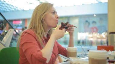 Şişman bir kadın bir kafede bir kek yiyor ve kahve sips