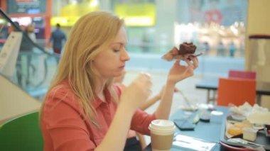 Şişman bir kadın bir kafede bir kek yiyor ve kahve sips