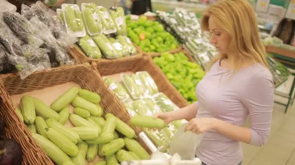 Een vrouw in een supermarkt op een plantaardige plank, het kopen van groenten, courgette — Stockvideo