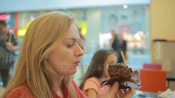En fet kvinna äter en cupcake på ett café och sips ner kaffe — Stockvideo