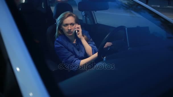Дівчина ввечері розмовляє по телефону, сидячи в машині — стокове відео
