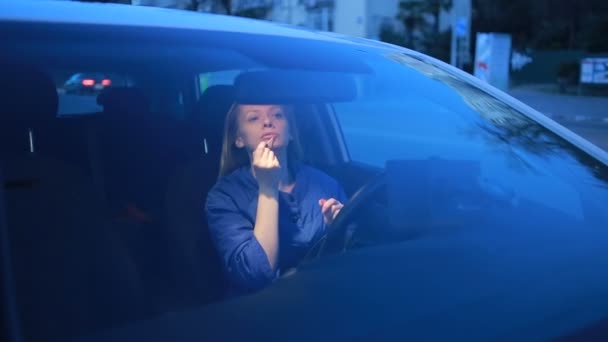 Дівчина малює губи блиском для губ, сидячи за кермом автомобіля — стокове відео