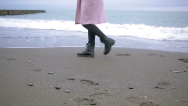 Gelukkig meisje in roze jas in de buurt van de zee tijdens een storm. Zee wast zijn voetafdrukken in het zand — Stockvideo