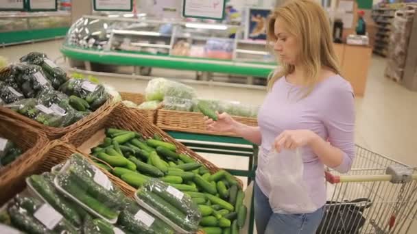 Een vrouw in een supermarkt op een plantaardige plank, groenten kopen. Komkommer — Stockvideo