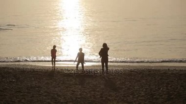 Gün batımında deniz kıyısında insan siluetleri. kadın ve çocuk
