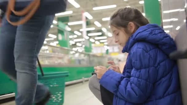 La hija y su madre están de compras en el supermercado. Pequeña ayudante amante — Vídeos de Stock