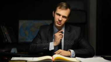 Kötü iş adamı, resmi, tehditkar bir şekilde ofis masasında otururken kameraya bakıyor