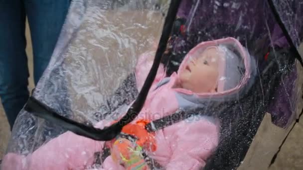 Maman et papa jouent avec leur bébé assis dans une poussette : protection contre la pluie — Video