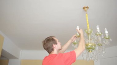 Yakışıklı erkek gömlek bir ampul bir kristal lamba için değiştirir.
