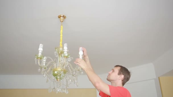 Uma camisa de homem bonito muda uma lâmpada para uma lâmpada de cristal — Vídeo de Stock