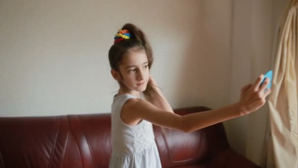 Маленькая девочка делает селфи на смартфоне дома на диване — стоковое видео