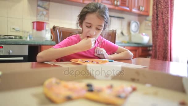 Дівчина їсть піцу та фрукти, граючи з телефоном на кухні за столом — стокове відео