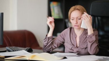Bir bilgisayar ve Office belgeleri ile çalışan çekici kadın telefonda konuşurken