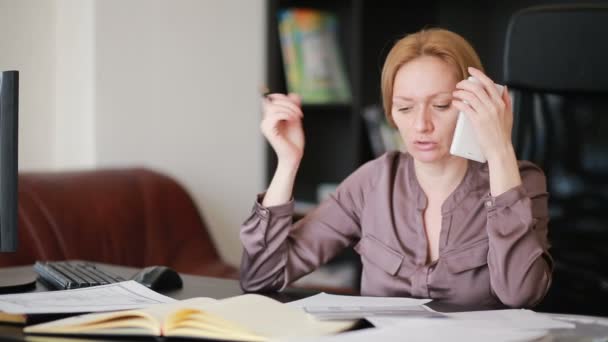 Attraente donna d'affari che lavora con un computer e documenti in ufficio, parlando al telefono — Video Stock