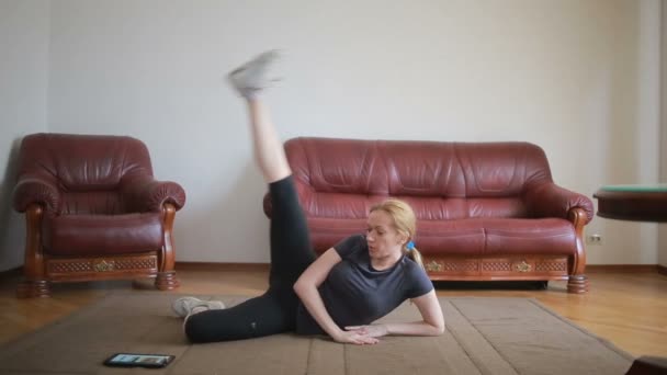 Een huisvrouw vrouw doet fitness oefeningen voor de eerste keer, het Tablet PC en de Tv kijken, is het moeilijk en onbekend, ze is moe. — Stockvideo