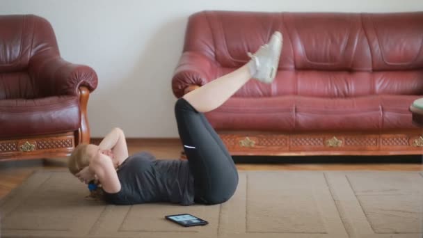Uma mulher dona de casa faz exercícios de fitness pela primeira vez, olhando para o tablet e TV, é difícil e desconhecido, ela está cansada. Instrução . — Vídeo de Stock