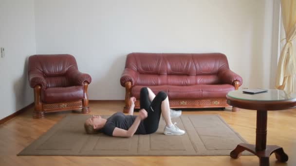 Una mujer ama de casa hace ejercicios de acondicionamiento físico por primera vez, mirando la tableta y la televisión, es difícil y desconocido, ella está cansada . — Vídeos de Stock