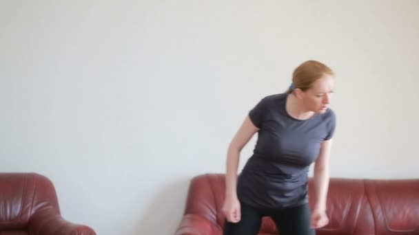 A housewife woman does fitness exercises for the first time, looking at the tablet and TV, it is difficult and unfamiliar, she is tired. — Stock Video