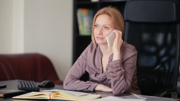 Atractiva mujer de negocios que trabaja con una computadora y documentos en la oficina, hablando por teléfono — Vídeo de stock