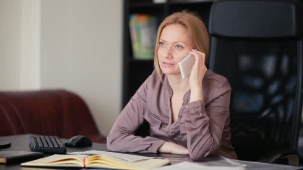 Attractive business woman working with a computer and documents in the office, talking on the phone — Stock Video