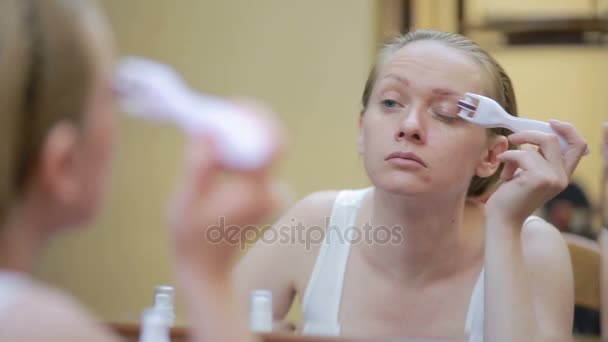Мезотерапия дома. Девушка мезороллером обрабатывает лицо дома перед зеркалом — стоковое видео