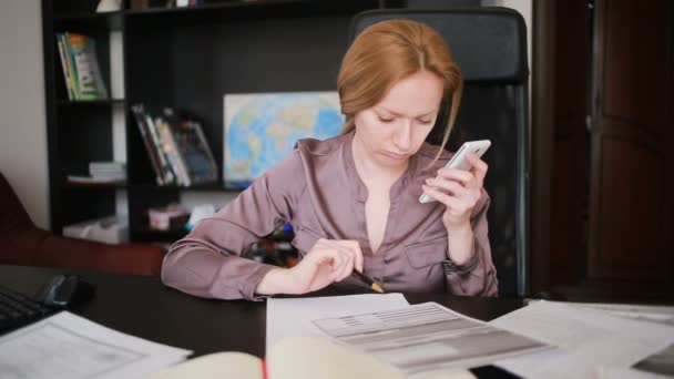 Mulher de negócios atraente trabalhando com um computador e documentos no escritório, falando ao telefone — Vídeo de Stock