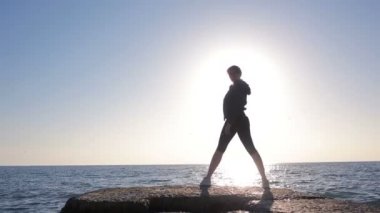 Genç kız plajda, suya yakın iskelede jimnastik yapıyor