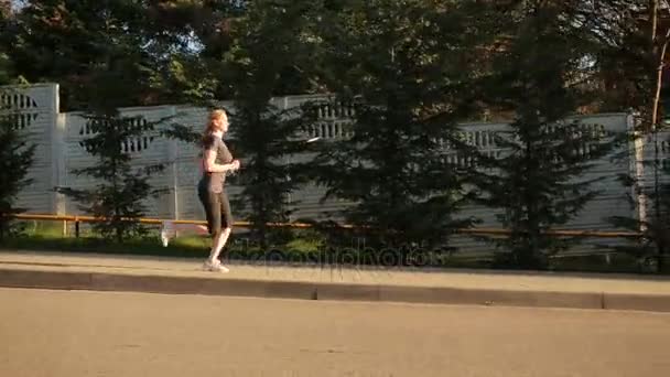 A female athlete runs on an asphalt alley in a park. — Stock Video