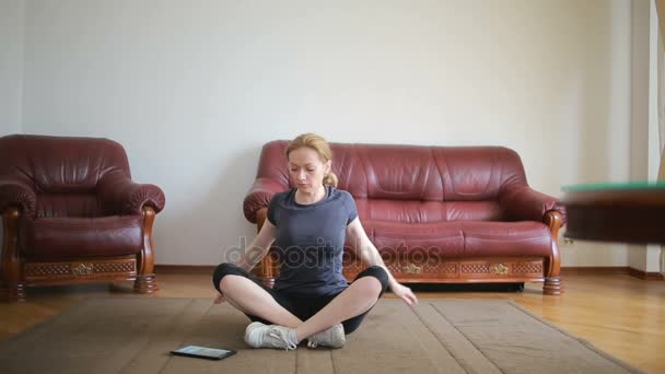 Una mujer ama de casa hace ejercicios de acondicionamiento físico por primera vez, mirando la tableta y la televisión, es difícil y desconocido, ella está cansada . — Vídeos de Stock