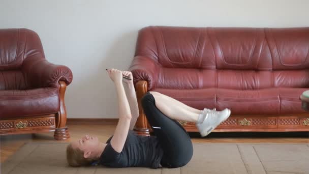Uma mulher dona de casa faz exercícios de fitness pela primeira vez, olhando para o tablet e TV, é difícil e desconhecido, ela está cansada. Instrução . — Vídeo de Stock