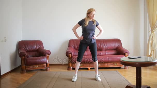 Een huisvrouw vrouw doet fitness oefeningen voor de eerste keer, het Tablet PC en de Tv kijken, is het moeilijk en onbekend, ze is moe. — Stockvideo