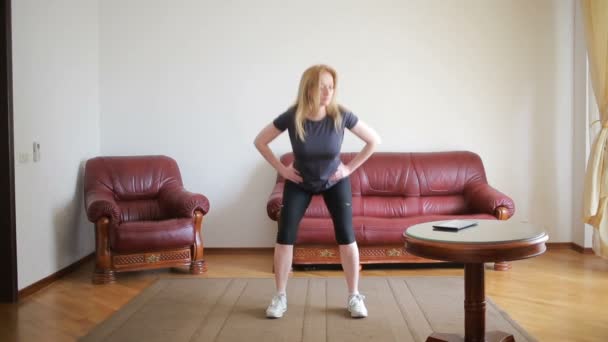En hemmafru kvinna gör fitnessövningar för första gången, tittar på tabletten och Tv, det är svårt och obekant, hon är trött. — Stockvideo