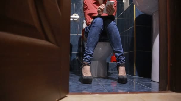 Vrouw zit in openbaar toilet. Met behulp van een smartphone, tablet — Stockvideo