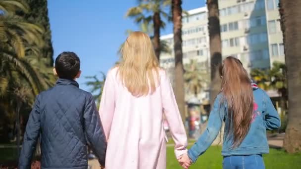 Žena s dětmi, matka drží dvojčata rukou procházky podél avenue s palmami — Stock video