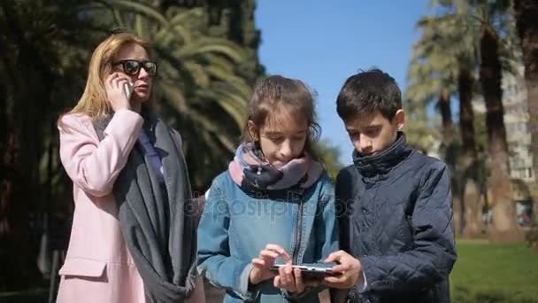 Женщина с детьми. Мама и дети идут по аллее, все заняты своим телефоном — стоковое видео
