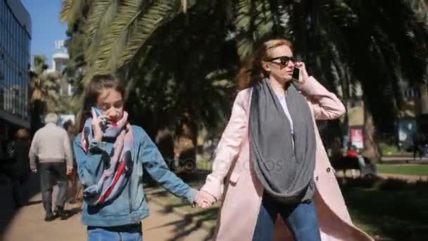 Женщина с детьми. Мама и дочь идут по аллее, все заняты своим телефоном — стоковое видео