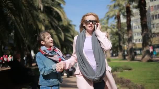 En kvinna med ett barn, en mamma som pratar i telefon, promenader längs gränden, ignorerar meddelandet av dottern, dotter kräver mödrar uppmärksamhet — Stockvideo