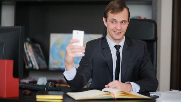 Привабливий бізнесмен розмовляє по телефону, роблячи селфі в офісі — стокове відео