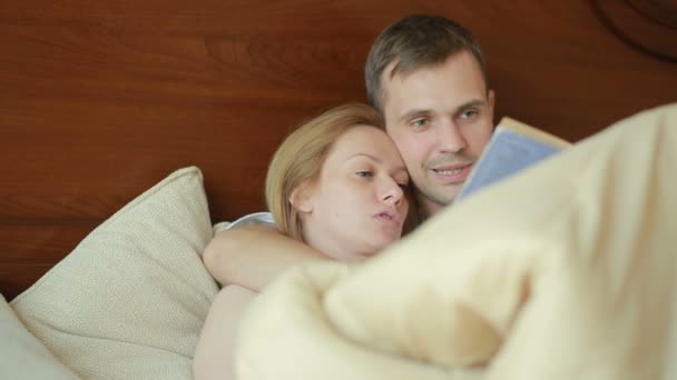 Ζευγάρι άνδρας και γυναίκα βρίσκονται στο κρεβάτι στην κρεβατοκάμαρα και διαβάσουμε μαζί το βιβλίο δυνατά — Αρχείο Βίντεο