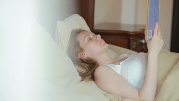 Beautiful young woman reading a sad book in bed — Stock Video