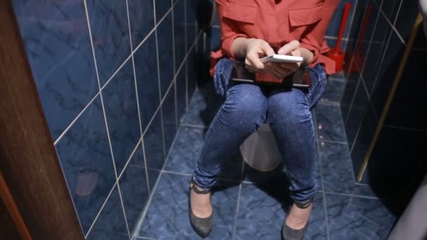 Žena sedí na veřejných WC. Pomocí chytrého telefonu, tabletu