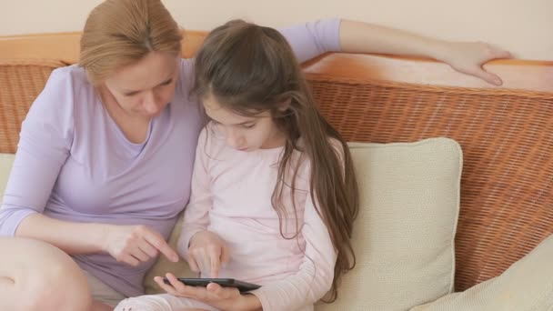 Egy gyönyörű anya és vele a kis lányom beszélni is, az anya tart egy tablettát, és tanítja a lányát — Stock videók