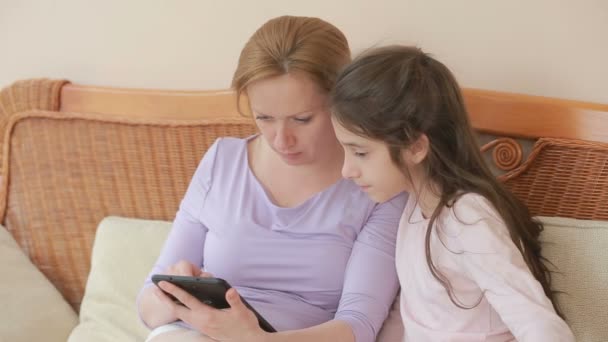 Eine schöne Mutter und ihre kleine Tochter sprechen gut, die Mutter hält ein Tablet und lehrt ihre Tochter — Stockvideo