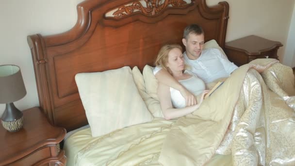 Mann und Frau liegen auf dem Bett im Schlafzimmer und lesen gemeinsam das Buch vor — Stockvideo