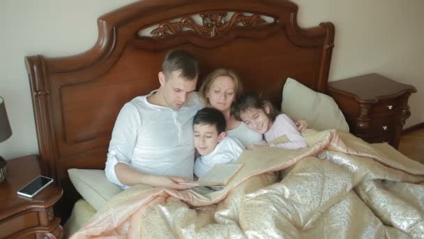 Família feliz na cama lendo um livro em voz alta em casa — Vídeo de Stock