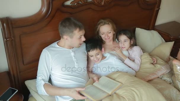 Familia feliz en la cama leyendo un libro en voz alta en casa — Vídeo de stock